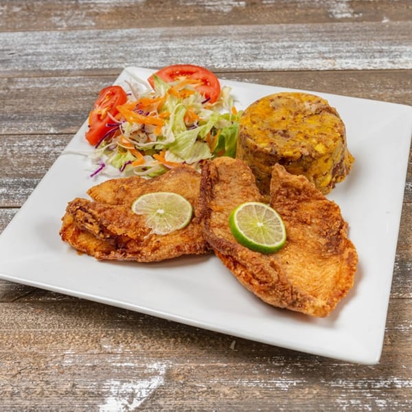 Fried fish with lime slices, a side of mofongo, and a fresh garden salad on a white plate.