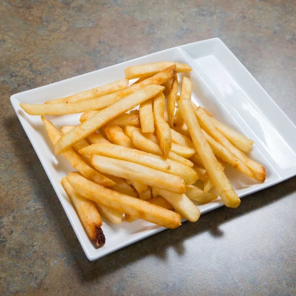 Golden-brown french fries piled on a white rectangular plate with two sections, on a speckled brown table.