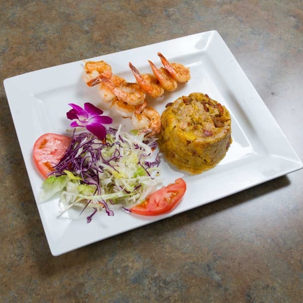 Mofongo with shrimp skewers, a side salad, tomato slices, and a purple orchid garnish.