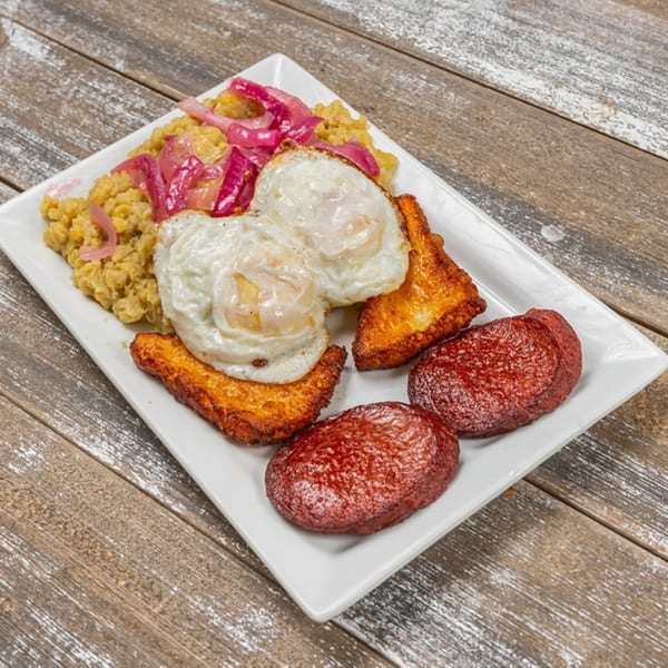 Mofongo with pickled red onions, fried eggs, fried cheese, and fried salami on a white plate.
