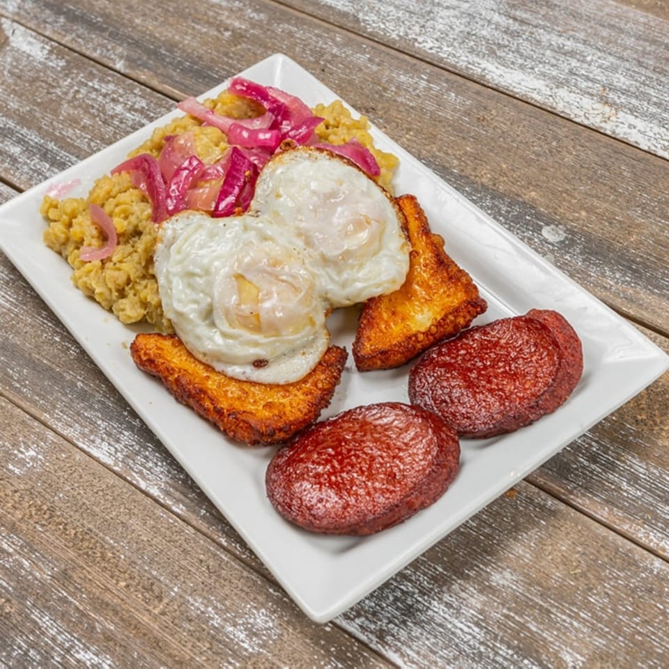 Mofongo with pickled red onions, fried eggs, fried cheese, and fried salami on a white plate.