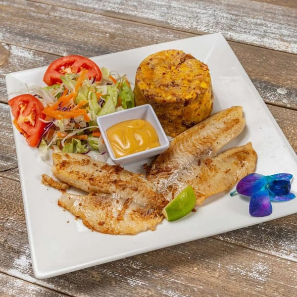 Mofongo with fried fish, a side salad, and a small dish of sauce on a white plate.