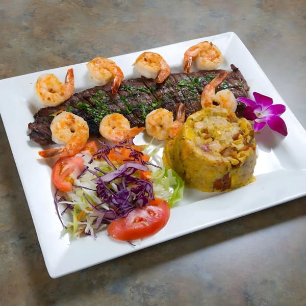 Mofongo with steak, shrimp, and a side salad, garnished with a purple orchid.